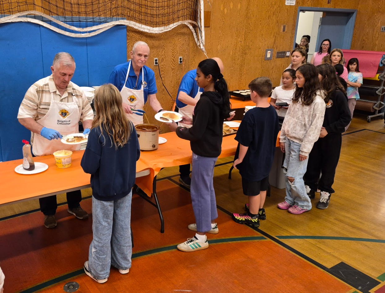 Serving pancakes to students lined up in the gym
