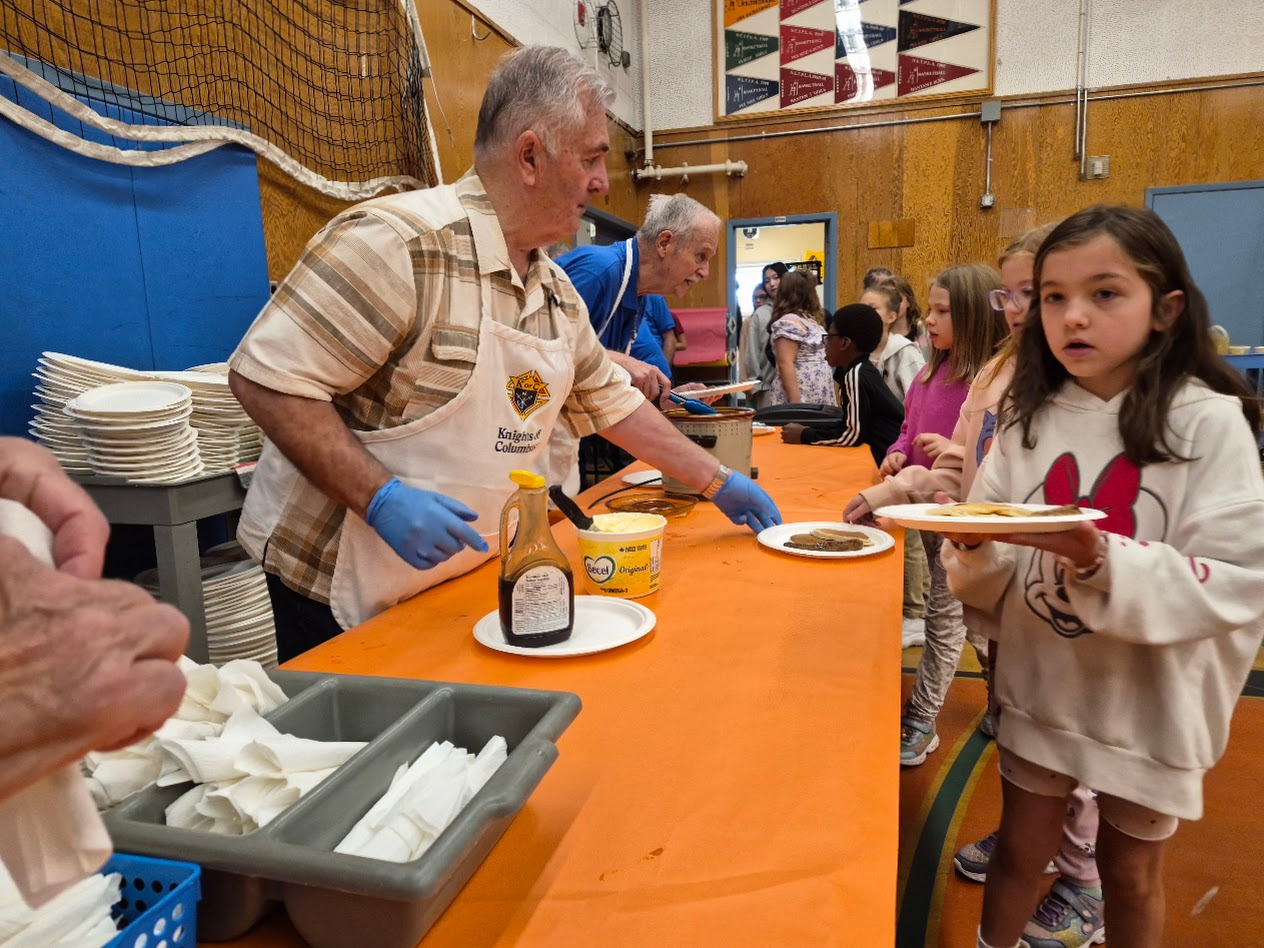 A Brother Knight serving a plate of pancakes to a student